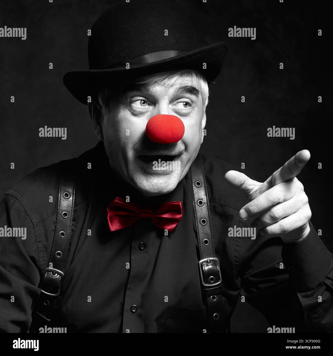 Selektives Farbporträt des lachenden Clowns. Ein älterer Mann mit roter Clownnnase und Bowler-Hut auf dem Kopf. In einem schwarzen Hemd mit Hosenträgern gekleidet. Der Clo Stockfoto