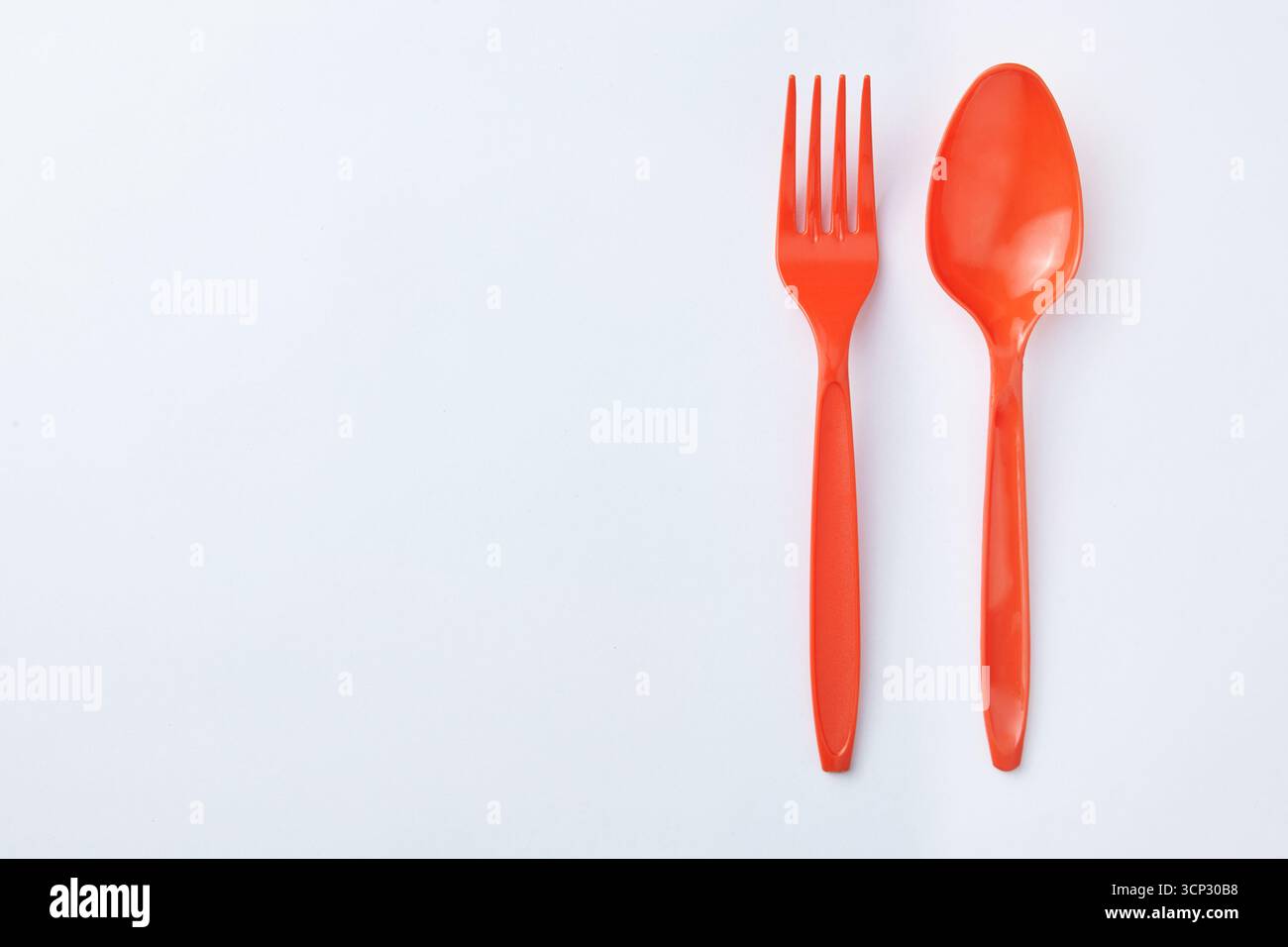 Rote Kunststofflöffel und -Gabeln werden nebeneinander auf einem sauberen weißen Hintergrund platziert, wodurch eine einfache und minimalistische, unausgewogene Komposition entsteht. Stockfoto