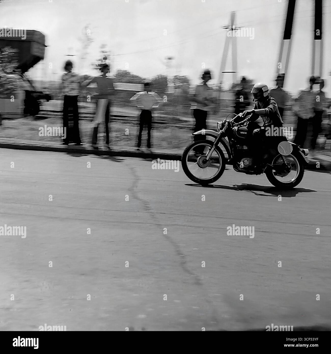 Ein hervorragender Schwenkschuss aus dem Jahr 1980 zeigt einen sowjetischen Motorradrennfahrer, der bei einem Straßenrennen in Sloviansk, der ukrainischen SSR, mit hoher Geschwindigkeit antritt. Der Fahrer und sein Vintage-Rennrad werden scharf im Fokus gehalten, während der Hintergrund mit Zuschauern, die die Straße säumen, mit Bewegungsunschärfen übersät ist, die die aufregende Geschwindigkeit des Ereignisses kraftvoll zum Ausdruck bringen. Dieses Schwarzweiß-Foto ist ein brillantes Beispiel für Action-Motorsport-Fotografie aus der UdSSR Stockfoto