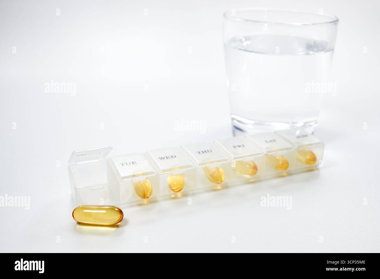 Ein wöchentlicher Pillen-Organisator zeigt eine tägliche Dosis von gelben Softgel-Ergänzungen wie Fischöl oder Vitamin E. Ein Konzept für das Gesundheitsmanagement, tägliche Routin Stockfoto