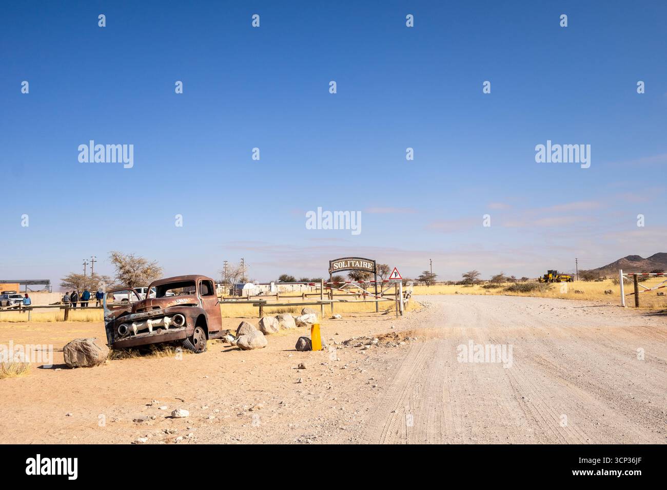 Auf dem Autofriedhof von Solitaire in Namibia befinden sich rostige Oldtimer in der Nähe kleiner Wüstengebäude, die vor Dünen und Bergen liegen und den Charme der Wüste einfangen Stockfoto