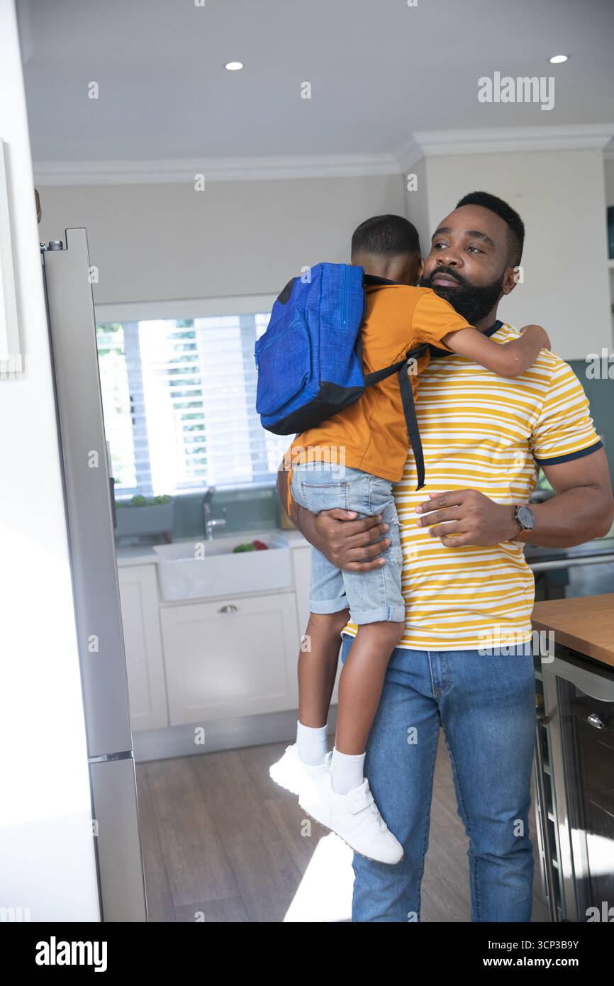 Afroamerikanischer Vater und Sohn umarmt in der Küche mit blauem Rucksack, Kopierraum Stockfoto