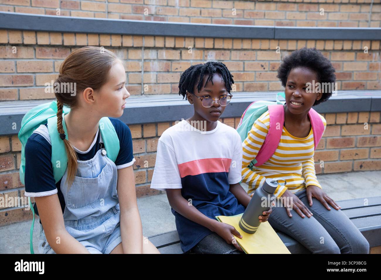 Verschiedene Klassenkameraden, die auf einer Tribüne sitzen, mit Rucksäcken, die ein Notebook mit Wasserflaschen halten Stockfoto
