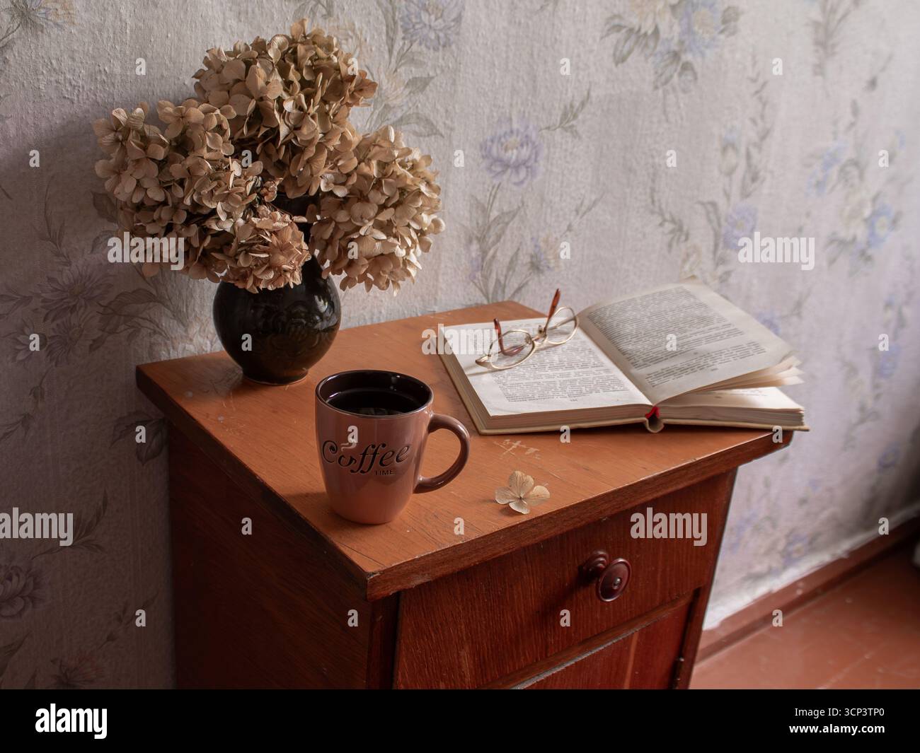Gemütliches Stillleben mit Kaffeetasse, offenem Buch und getrockneten Blumen auf einem Holztisch, Vintage-Inneneinrichtung. Stockfoto