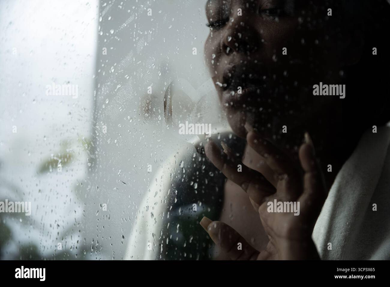 Eine Frau, die auf einem regendurchfluteten Fenster zeichnet, verloren in ihren Gedanken und Gefühlen. Stockfoto