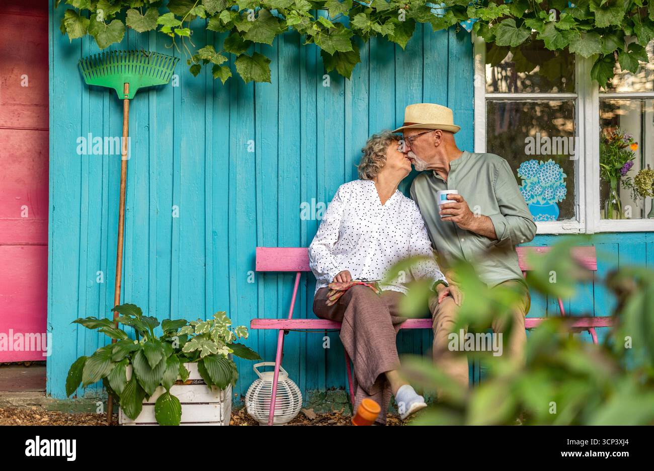 Ein älteres Paar küsst sich im Garten an einem sonnigen Tag Stockfoto
