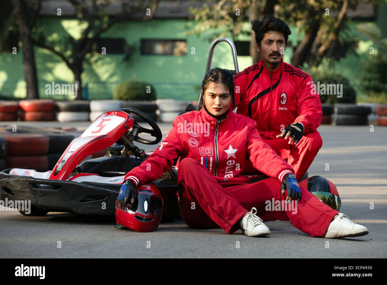 Ein stylisches Paar in roten Trainingsanzügen posiert mit einem Go-Kart auf einer Rennstrecke Stockfoto