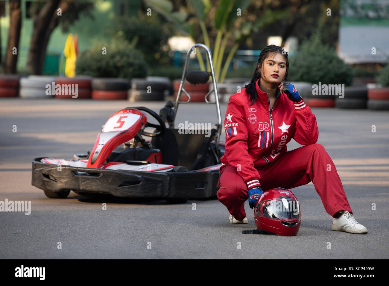 Eine weibliche Racerin, die sich neben einem Go-Kart mit ihrem Helm hockt Stockfoto