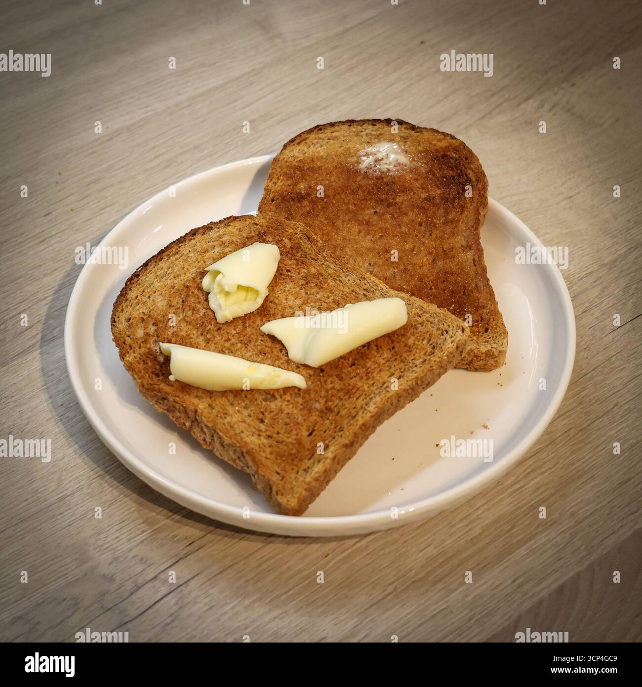 Warme gebutterte Scheiben Toast/geröstetes Brot auf einer weißen Platte, die in Butter getaucht ist und langsam schmilzt Stockfoto
