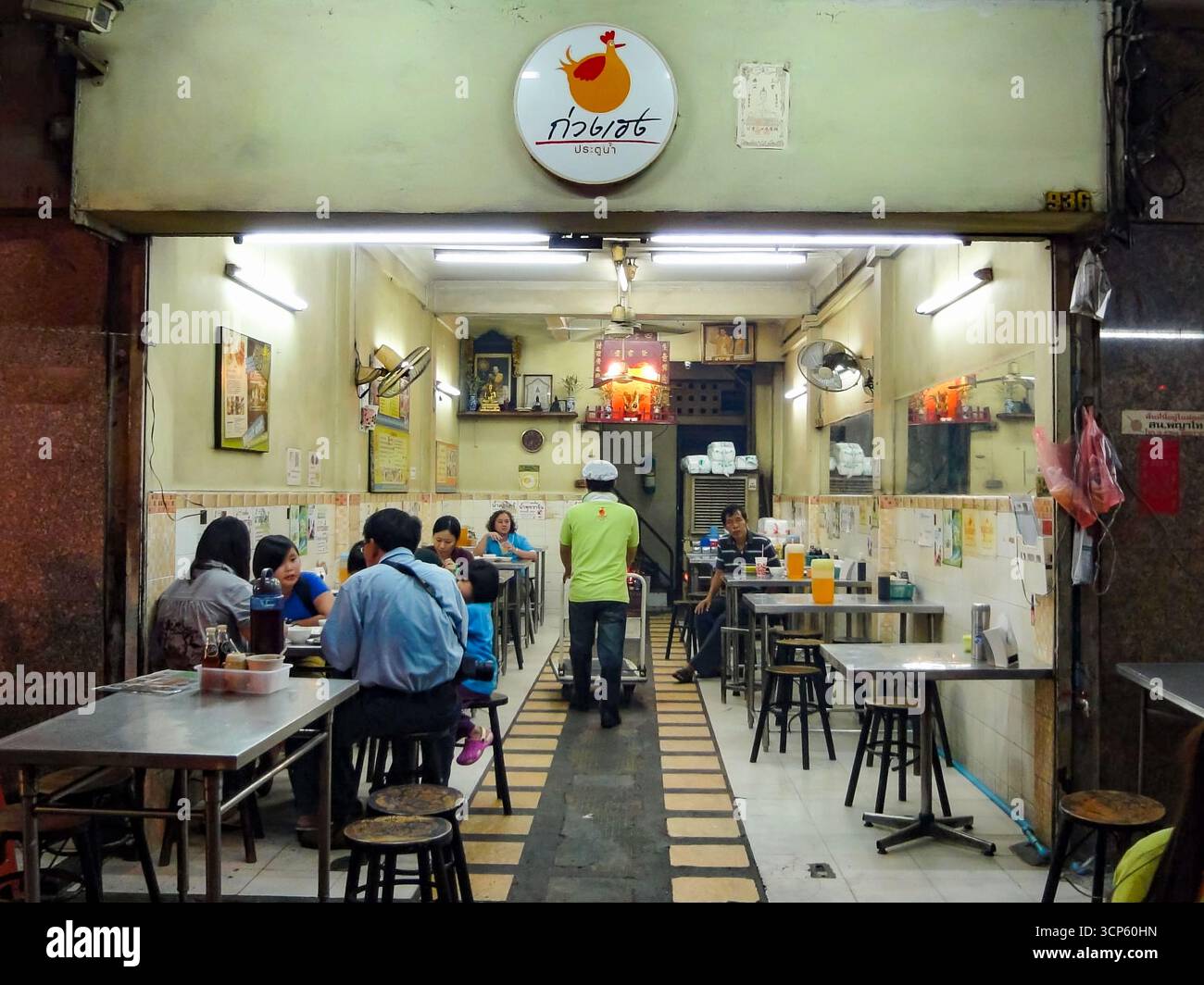Traditionelles thailändisches Street Food-Restaurant mit einheimischen Gerichten, Blick auf das Innere mit Tischen, Wandventilatoren und Altar-Dekor, Bangkok, Thailand. Stockfoto