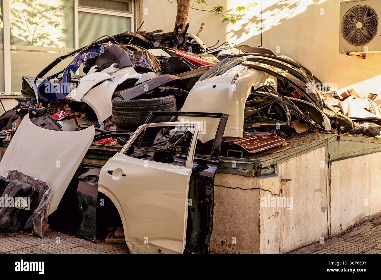 Stapel demontierter Autoteile und Fahrzeugfragmente, die im Freien durch eine Gebäudewand gestapelt werden. Konzept des Kfz-Recyclings, des Kfz-Abfalls und der Automobilindustrie Stockfoto