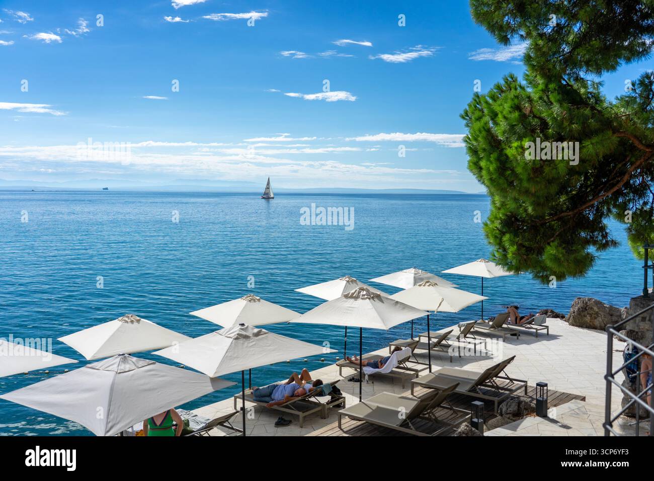 Opatija, Kroatien - 08.25.2025 : Terrasse am Meer mit Sonnenschirmen und Liegestühlen mit Blick auf das ruhige blaue Meer Opatija Kroatien. Stockfoto