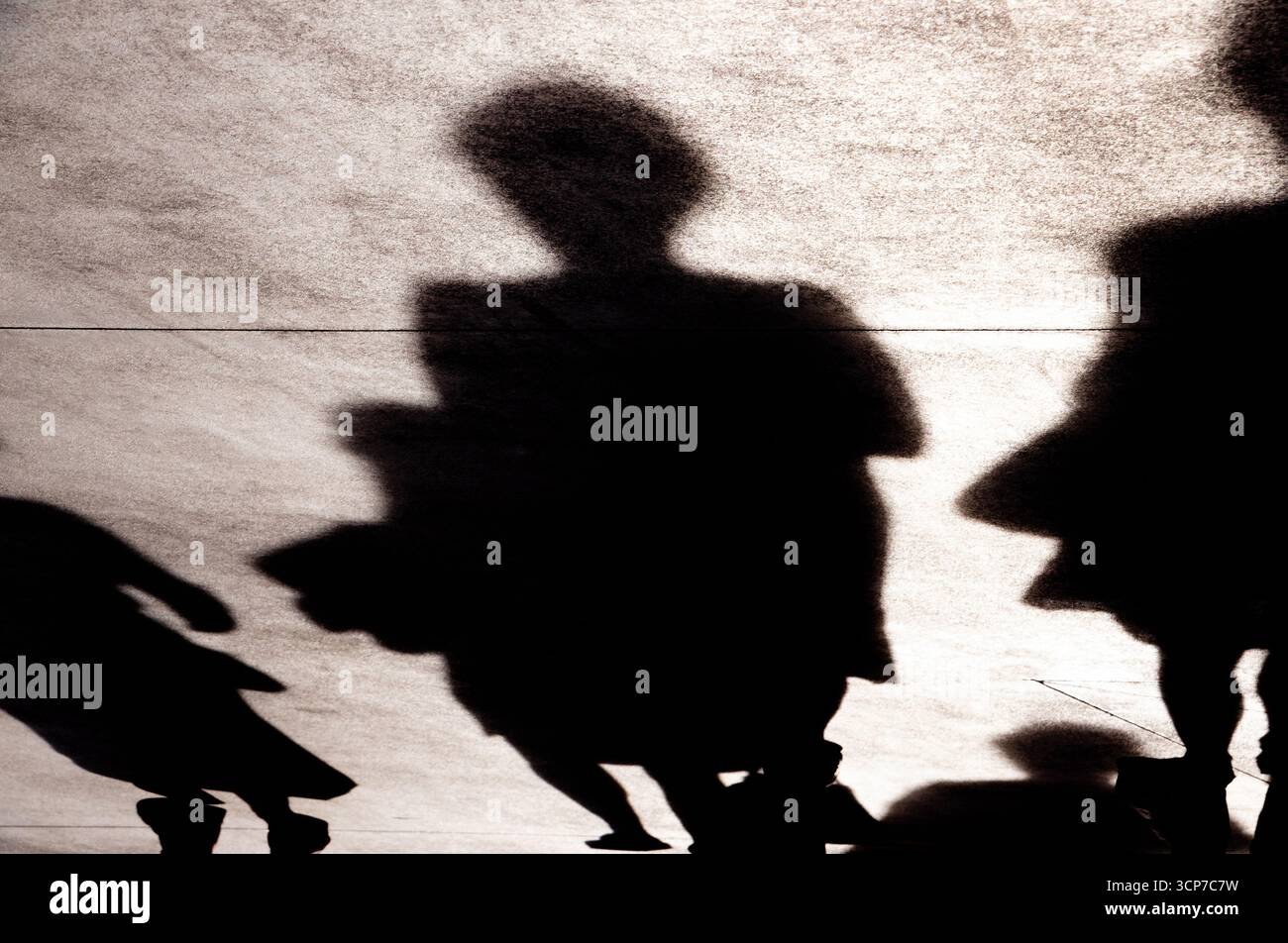 Schatten-Silhouette von Fußgängern, die in einer Sommersonne auf der Straße spazieren gehen, in Sepia-Schwarz-weiß Stockfoto