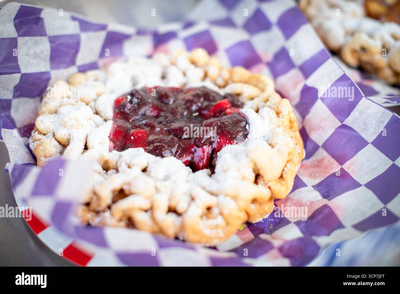 FREDERICK Fairgrounds Frederick Maryland // FREDERICK, Maryland — Ein Trichterkuchen mit Erdbeerkonserven und Puderzucker wird auf der Great Frederick Fair in einem lila-weiß karierten Papierfutter serviert. Die Messe findet jährlich auf den Frederick Fairgrounds in Frederick, Maryland, USA statt. Stockfoto