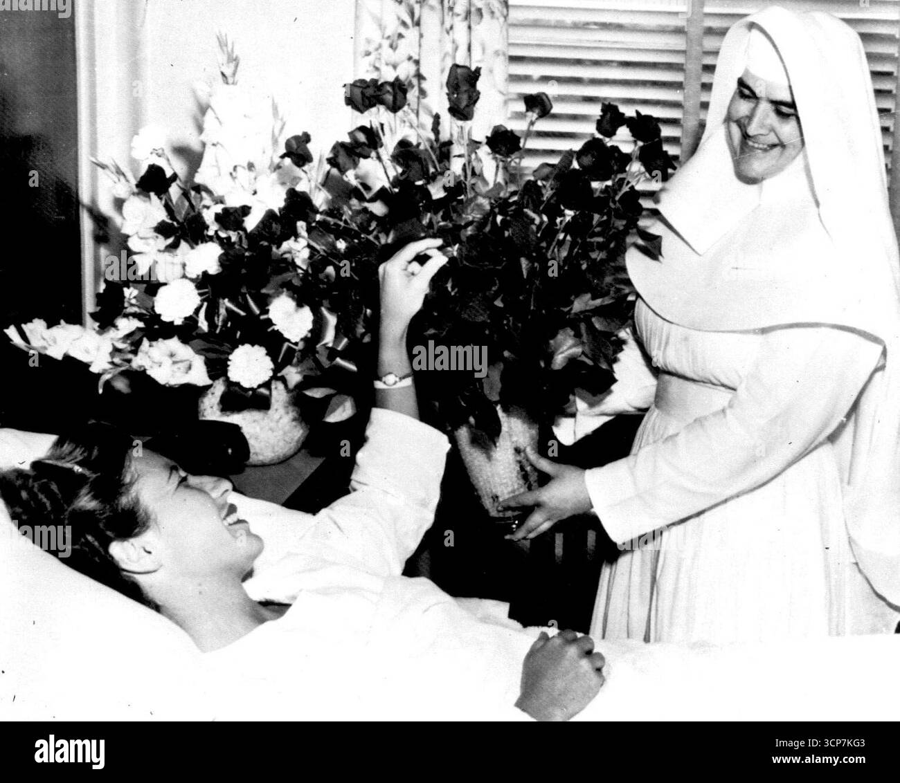 Blumen für die Königin - Tennis Queen Maureen Connolly bewundert vier Dutzend Rosen, die heute von Schwester von Mercy gehalten werden. "Little Mo" erlitt ein gebrochenes und ernsthaft geschnittenes Bein, als ihr Pferd, das sie gescheut reitet, gestern gegen einen Zementwagen warf. Juli 1954. (Foto von AP Wirephoto). Stockfoto