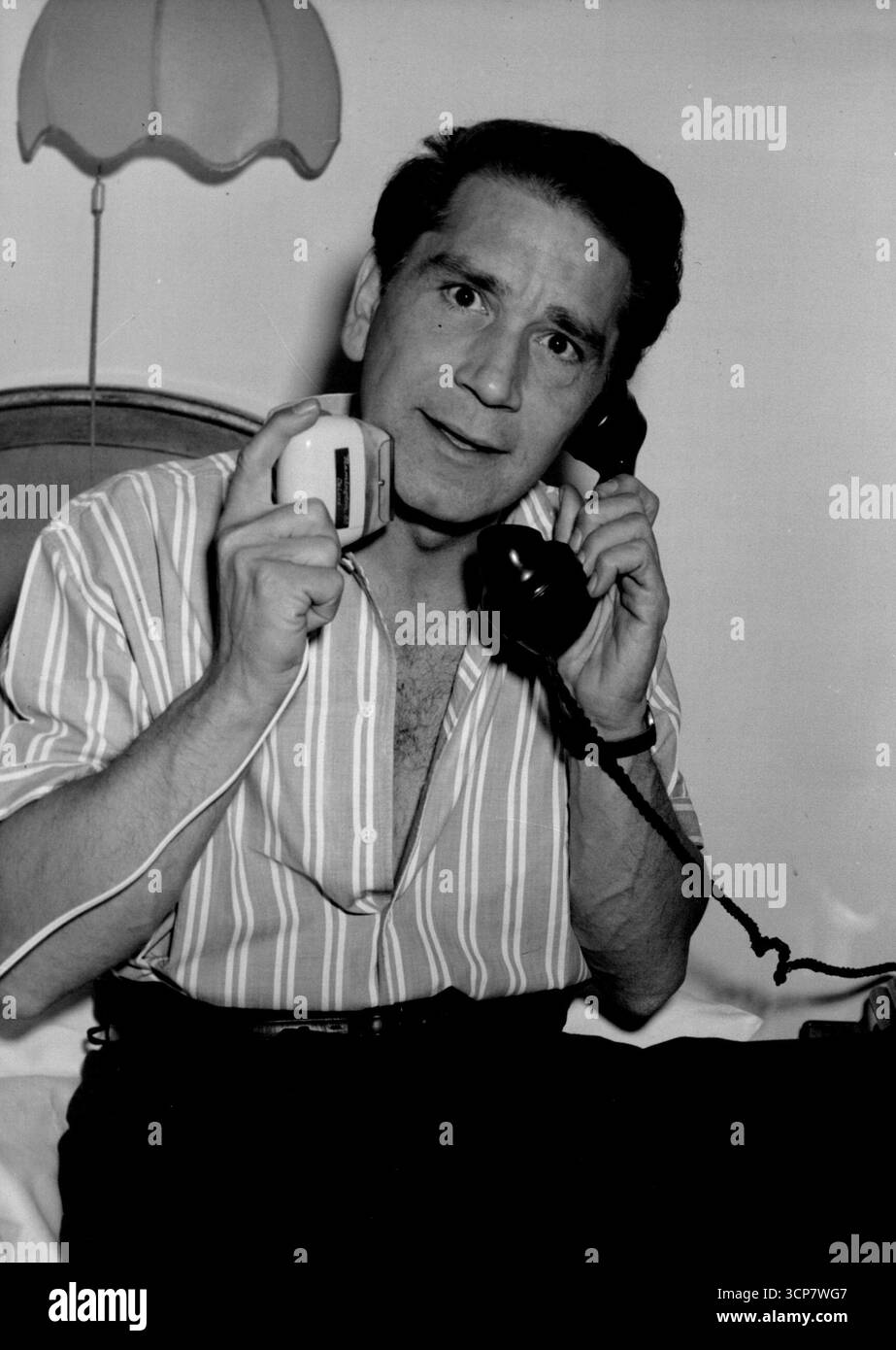 Conte-der harte Kerl kommt, der Mann in Aktion. Mit einer Hand rasiert er sich, mit der anderen ruft er seine Frau in Hollywood über den atlantik an. Richard Conte, ein harter Hollywood-Schauspieler, kam heute in London an. Er ist hier, um mit der Arbeit an dem neuen Film „Mask of Dust“ zu beginnen, dessen Geschichte sich um den internationalen Autorennen dreht. Ein Großteil des Films wird auf der Rennstrecke im Goodwood Park in Sussex gedreht. In dem Film spielt Conte die Kanadierin Mari Aldon. Viele der führenden Rennfahrer werden ebenfalls vertreten sein, darunter Reg Parnell john cooper und Roy Salvadore Stockfoto