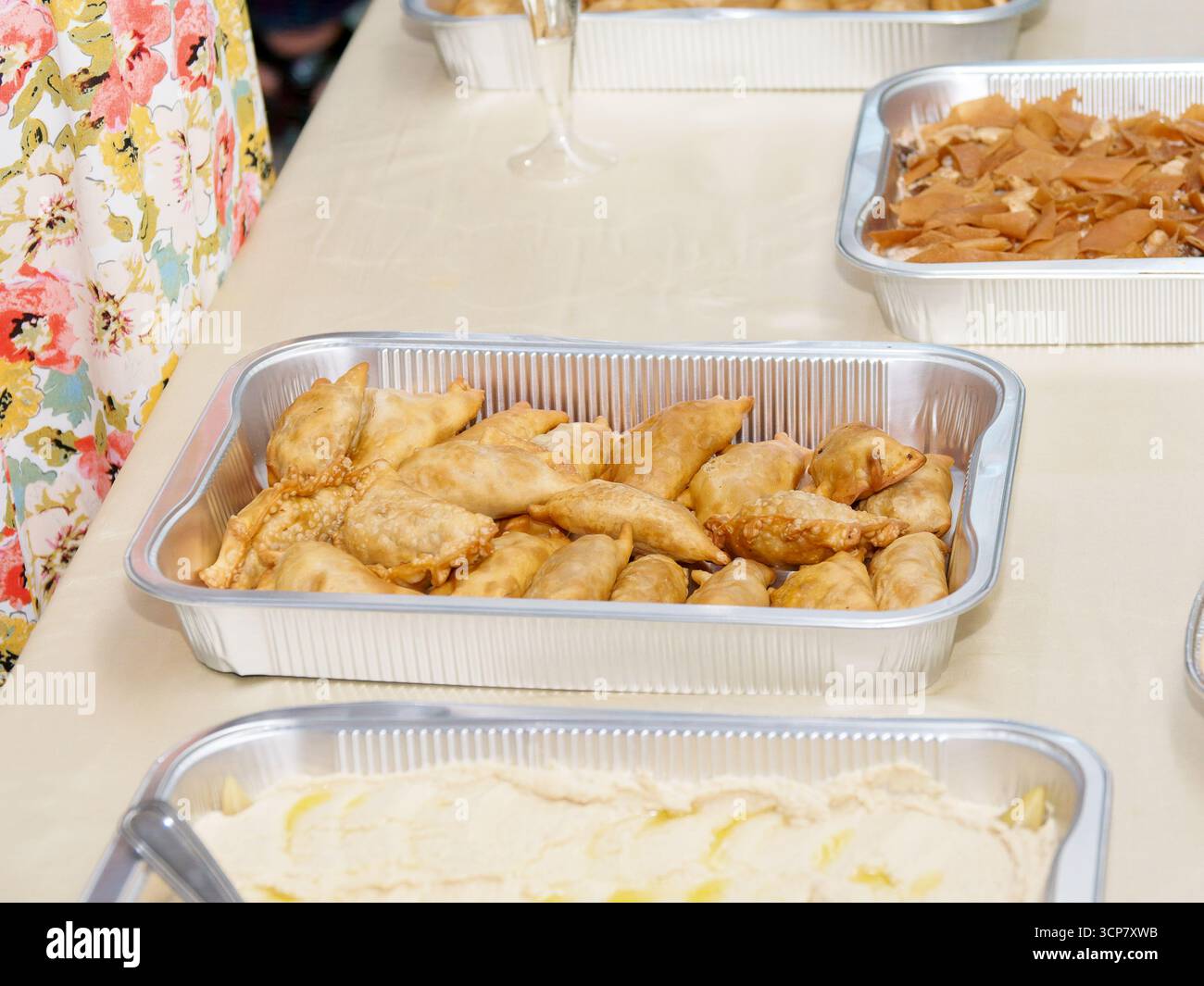 Gebratene Samosas auf Aluminiumtablett am libanesischen Mezze-Buffet mit Hummus und traditionellen Gerichten für Catering-Empfänge. Stockfoto