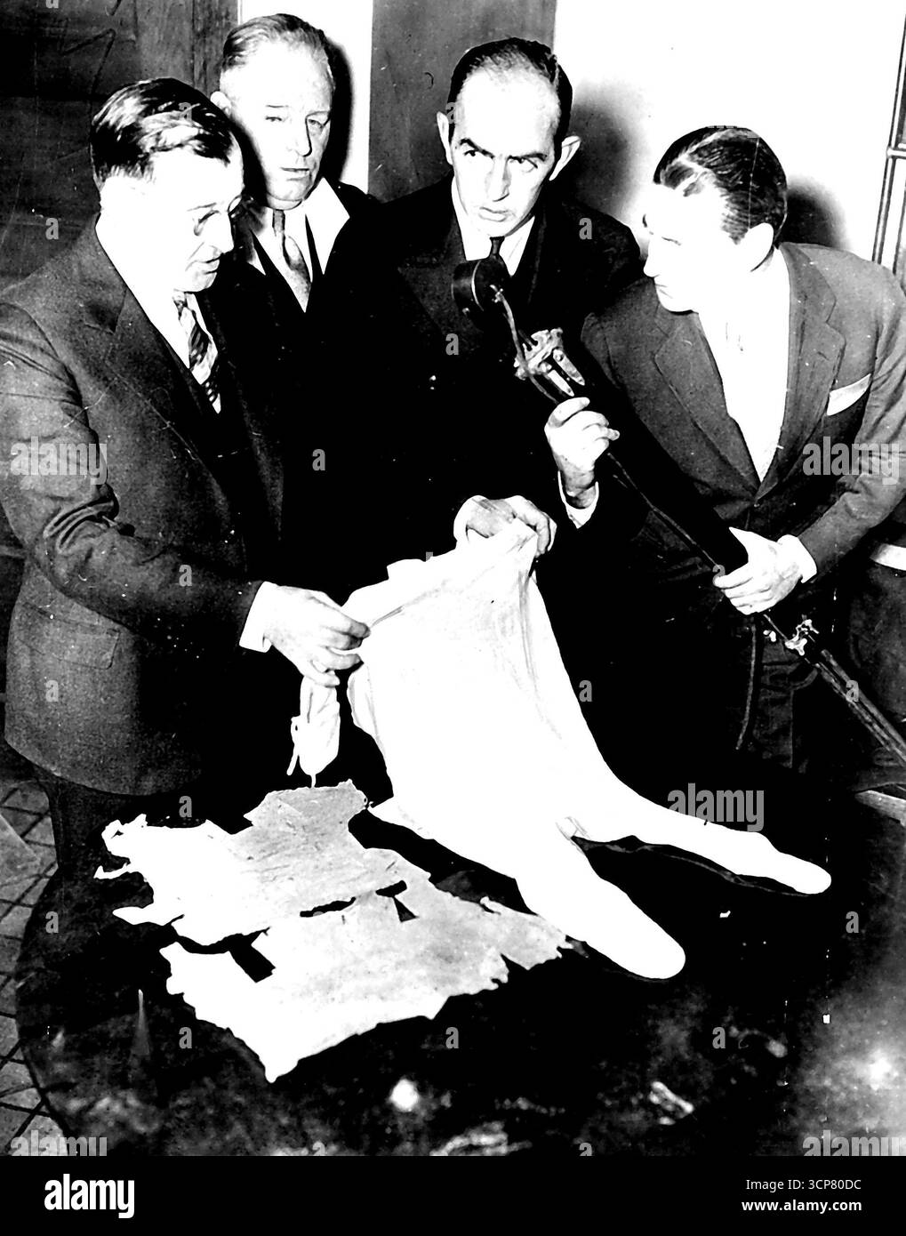 Kleidung, die vom ermordeten Lindbergh-Baby getragen wurde -- hier ist die Kleidung, die das Baby Charles A. Lindbergh in der Nacht vor fast drei Jahren trug, als Bruno Richard Hauptmann es entführt und ermordet haben soll. Von links nach rechts, Robert Peacock, stellvertretender Generalstaatsanwalt, Anthony Hauck, Staatsanwalt von Hunterdon, und Captain John Lamb von der Staatspolizei von N. J. untersucht die Kleidung, nachdem sie am 3. Januar als Beweis in Hauptmanns Prozess in Flemington, N.J., eingeführt wurde. Ein Mikrofontechniker für einen Newsreel-Kameramann ist ganz rechts. Januar 1935. (Foto von zugehörigem Pressefoto). Stockfoto