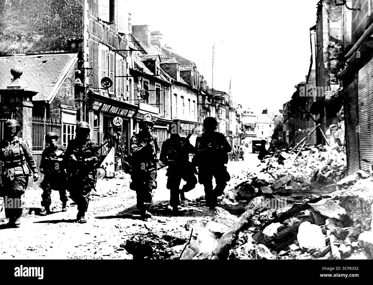 Amerikanische Truppen in Carentan -- amerikanische Truppen, die Scharfschützen warnen, drücken auf die zerstörten Gebäude in den Straßen von Carentan am Fuße der Cherbourg-Halbinsel. Nach zwei Tagen bitterer Kämpfe befreiten die amerikanischen Truppen der Alli & Expaditionary Force Carentan, dessen Besitz die Verbindung zwischen zwei großen Steilköpfen in alliierter Hand matarisch verstärkt. August 1944. Stockfoto