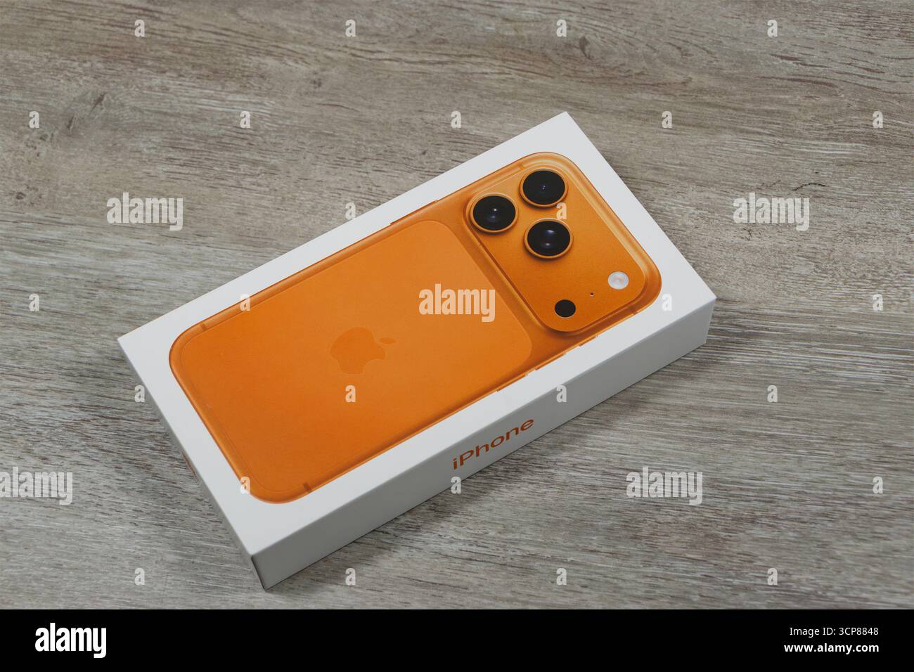 Orangefarbenes Smartphone mit drei Kameras in einer Box auf einer Holzoberfläche Stockfoto