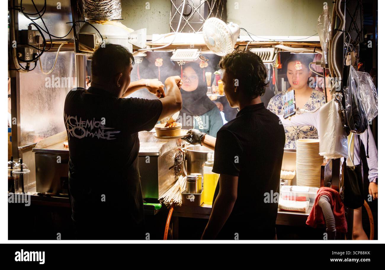 Straßenverkäufer servieren asiatische Speisen auf einem belebten malaysischen Nachtmarkt, lebhafte lokale Kultur malaysia Stockfoto