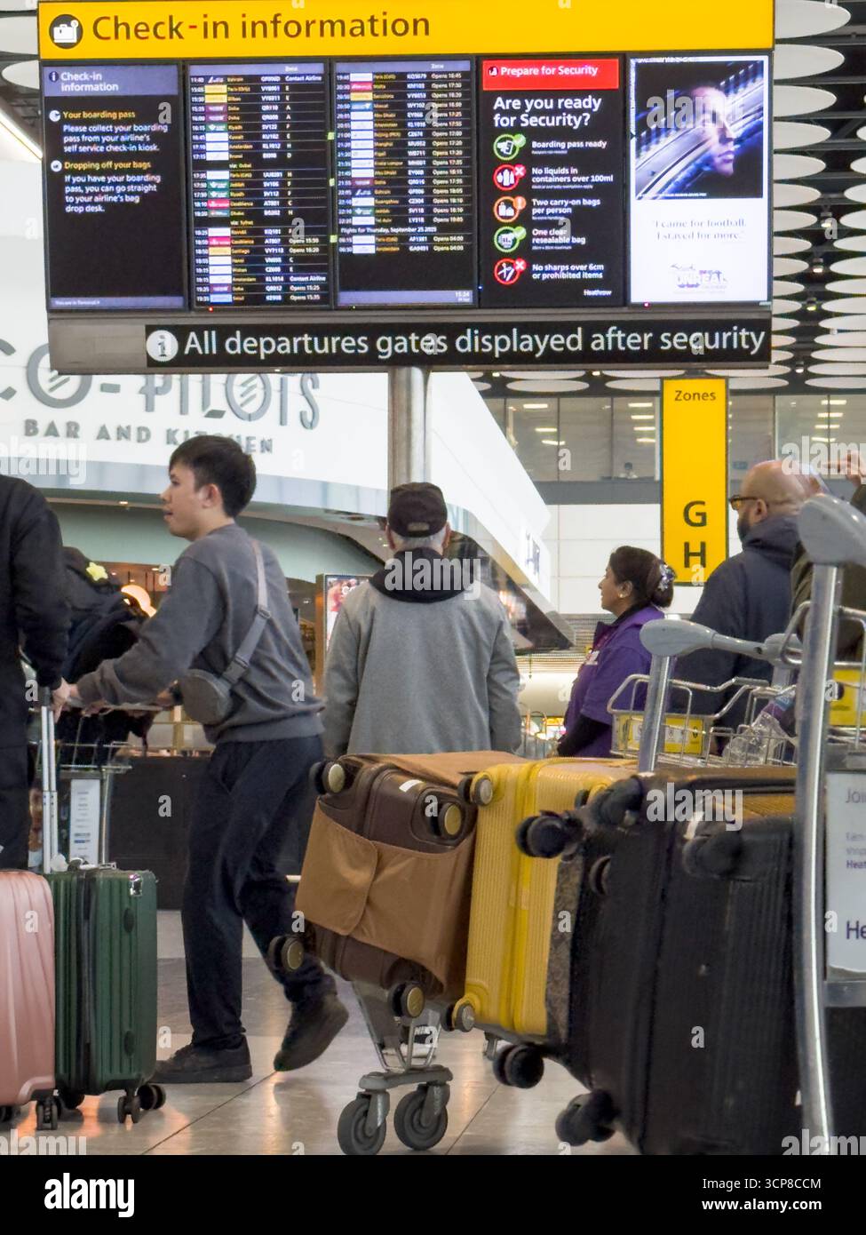 London Heathrow, Großbritannien – 24. September 2025: Fluggäste stehen in Warteschlange mit Gepäckwagen, während sie die Abflugbildschirme am Flughafen London Heathrow überprüfen Flüge vom Flughafen London Heathrow sind nach einem jüngsten Angriff auf die Flughafensoftware wieder normal. Quelle: Glosszoom/Alamy Live News. Stockfoto