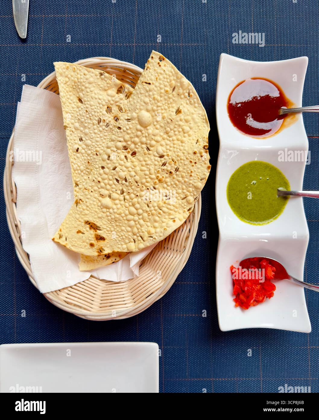 Papadum auf dem Servierkorb mit Saucen an der Seite auf einer blauen Tischmatte. - Smartphone-aufgenommenes Stockfoto