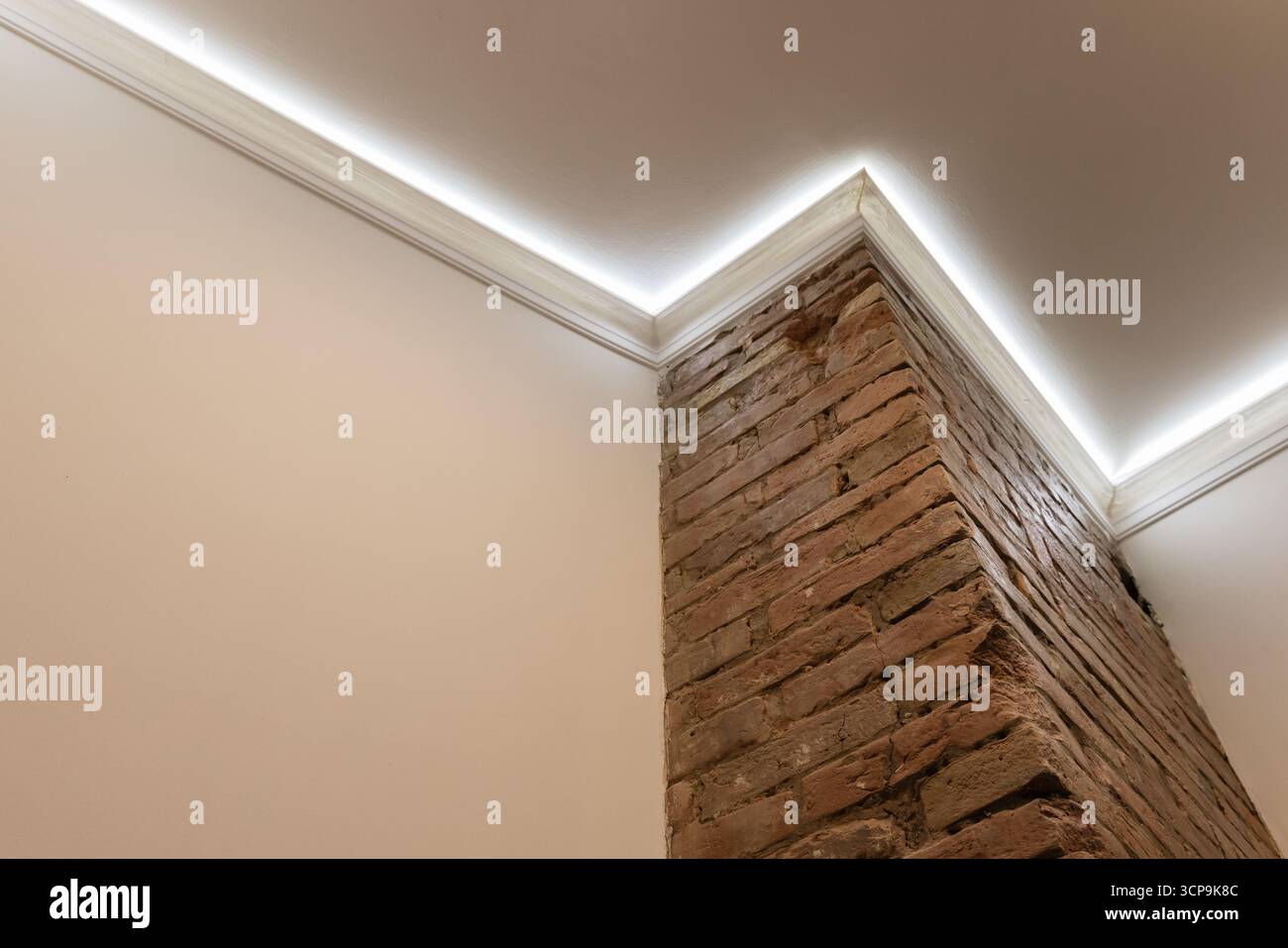 Eine moderne Einrichtung mit freiliegender Ziegelsäule, die von einer weißen Wand ragt und durch indirekte Beleuchtung in der Bucht sanft beleuchtet wird. Robuster Ziegelstein steht im Kontrast zu Stockfoto