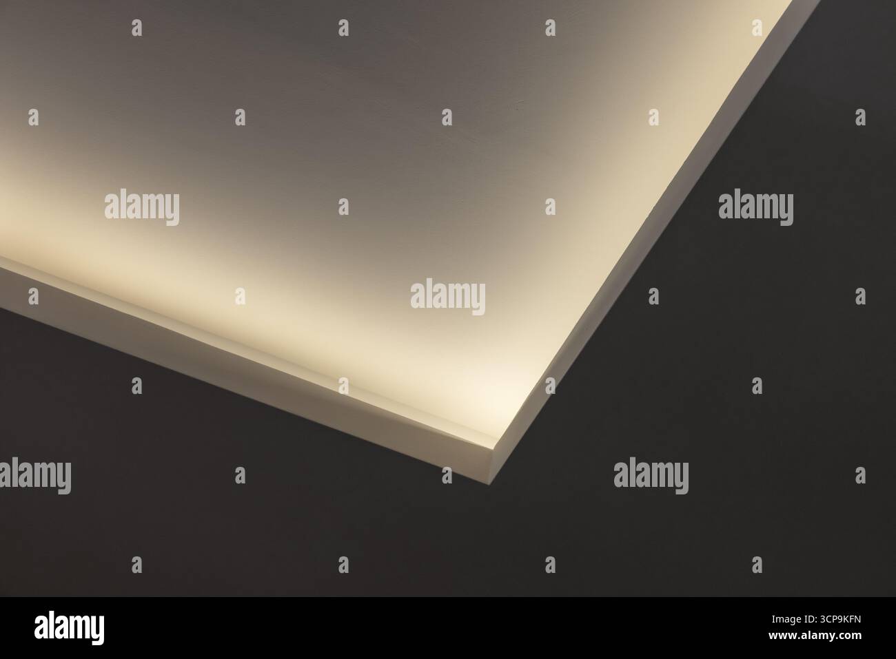 Eine minimalistische Nahaufnahme des Innenraums zeigt warme indirekte Beleuchtung entlang einer schrägen Deckenkante, die eine ruhige, skulpturale Stimmung schafft Stockfoto