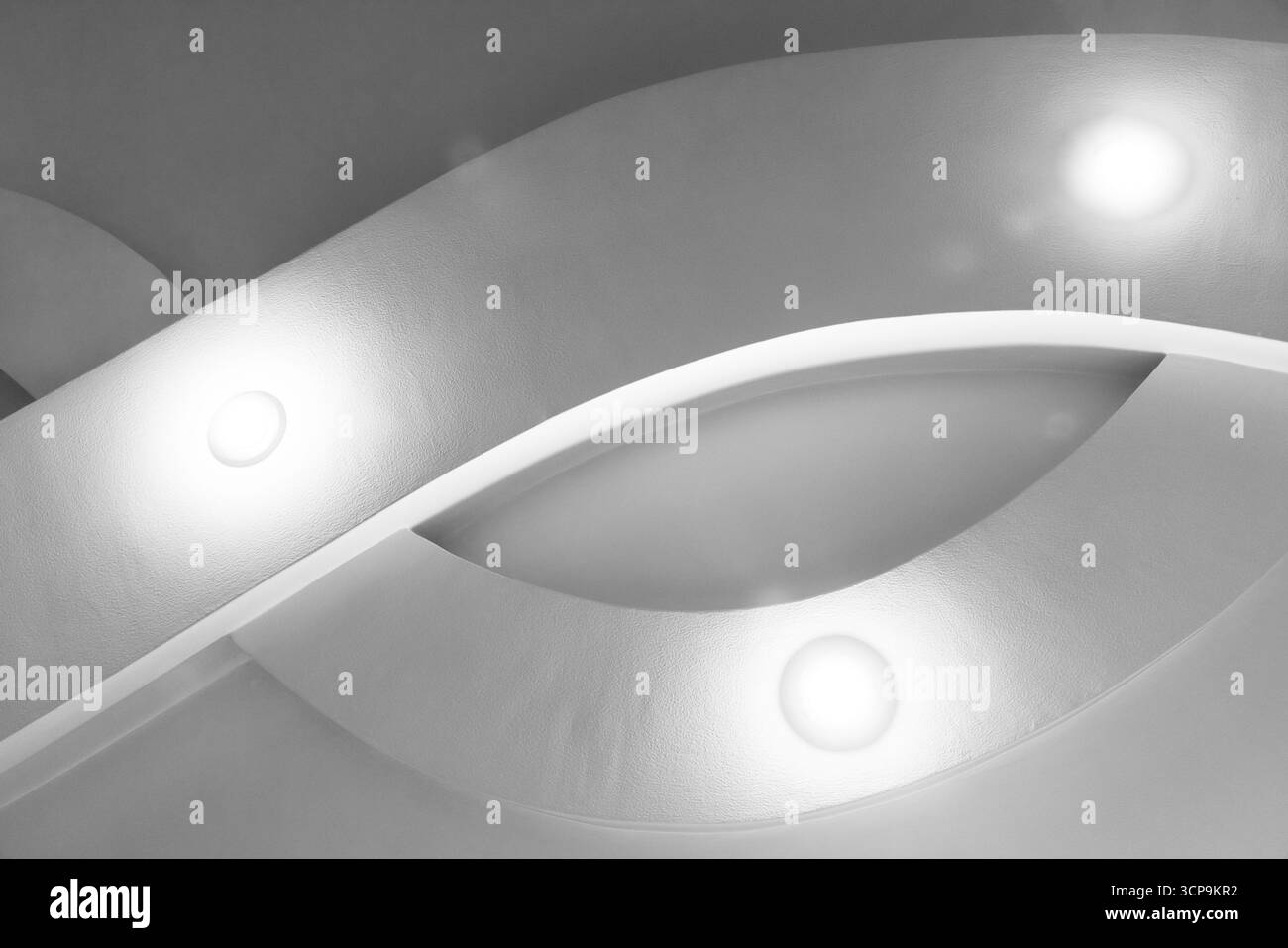 Eine abstrakte Architekturszene in Graustufen mit geschwungenen Oberflächen und Einbauleuchten, die sanftes Leuchten erzeugen. Saubere, moderne Linien vermitteln Ruhe und Raffinesse Stockfoto