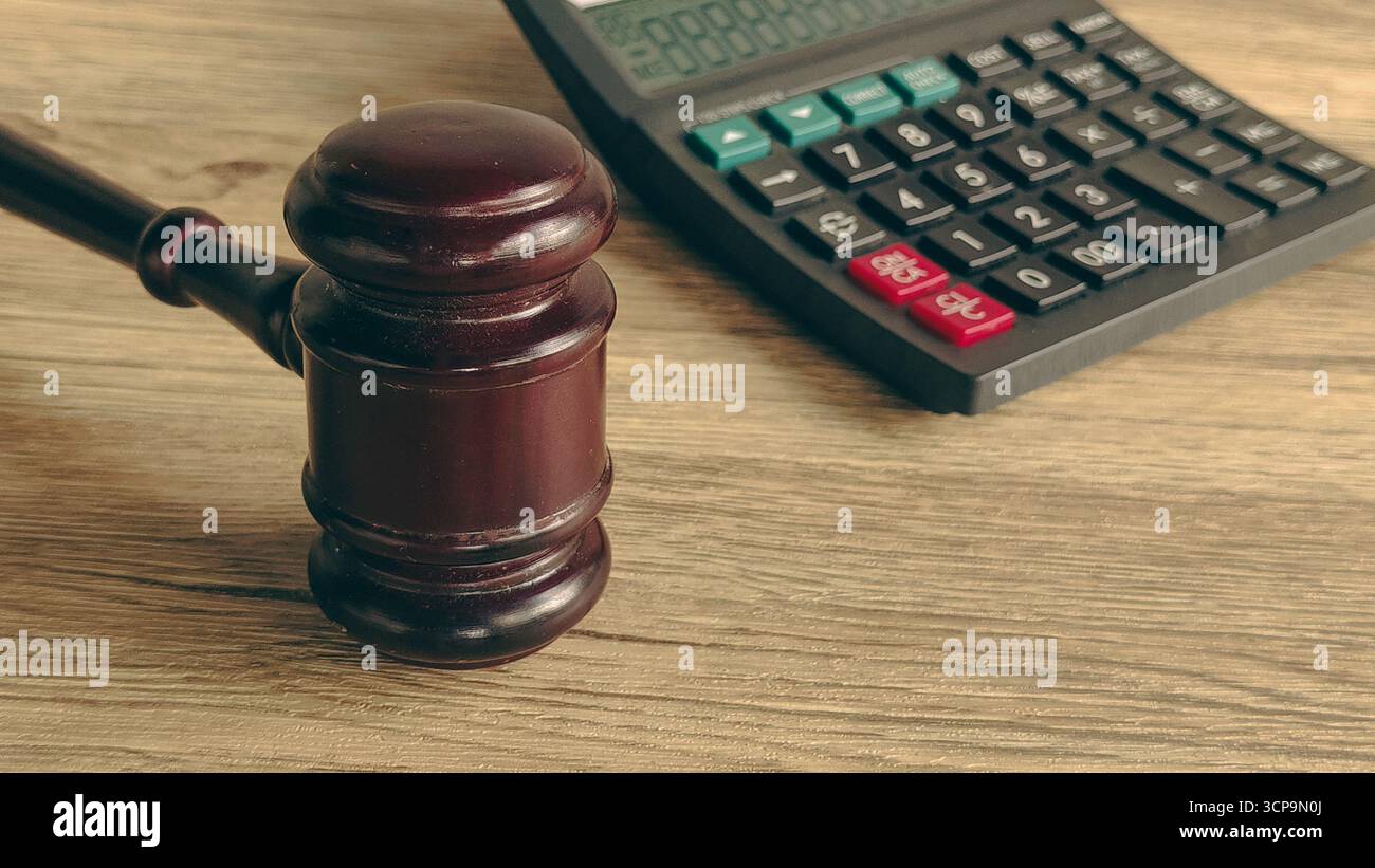 Hammer und Taschenrechner auf einem Holztisch, symbolisiert rechtliche Finanzen und Konsequenzen. Stockfoto
