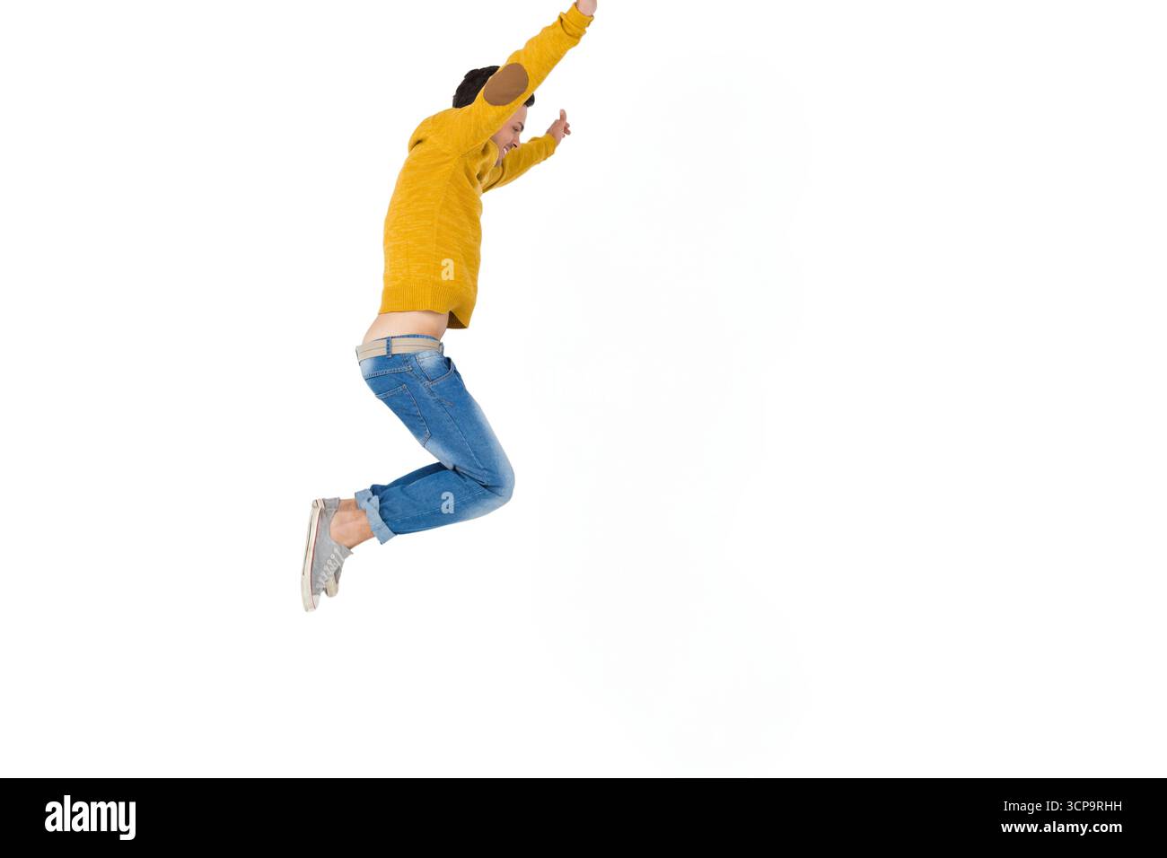 Mann springt energisch im Studio mit Senfpullover und Jeans, weißem Hintergrund, Kopierraum Stockfoto