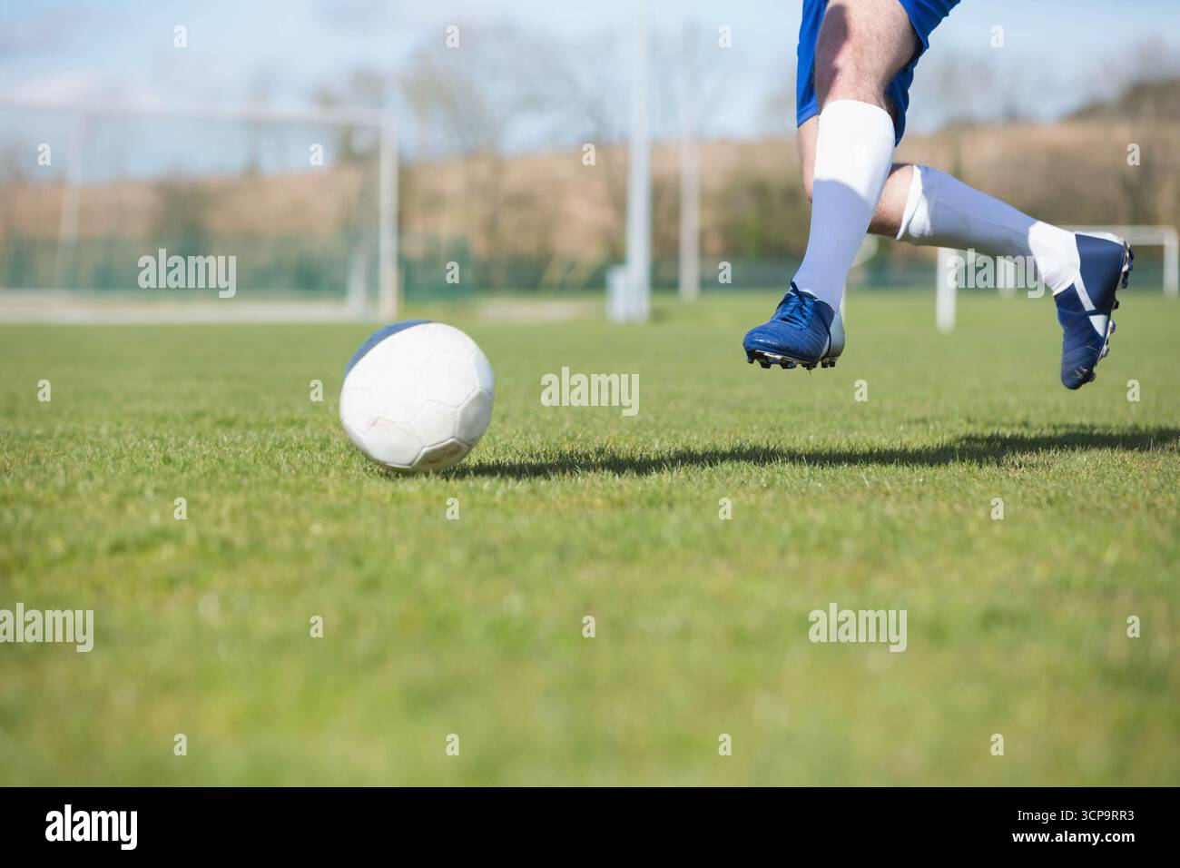 Männlicher Teenager-Fußballspieler mit blauen Stollen, der Fußball auf dem Feld in der Nähe von Torpfosten, Kopierraum tritt Stockfoto