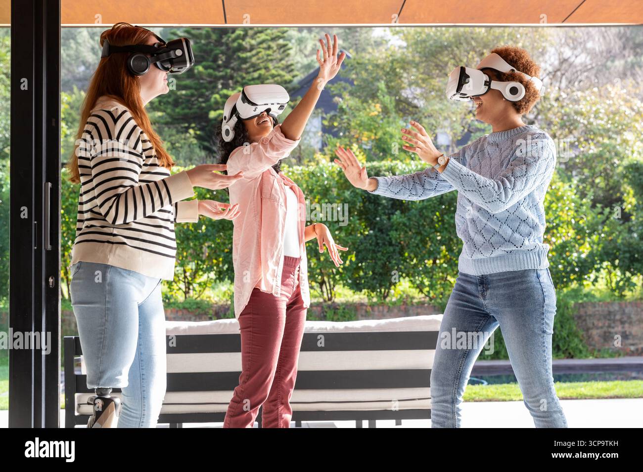 Verschiedene weibliche Freunde, die mit vr-Headsets in der Nähe des Arbeitsplatzes mit virtuellen Objekten interagieren Stockfoto