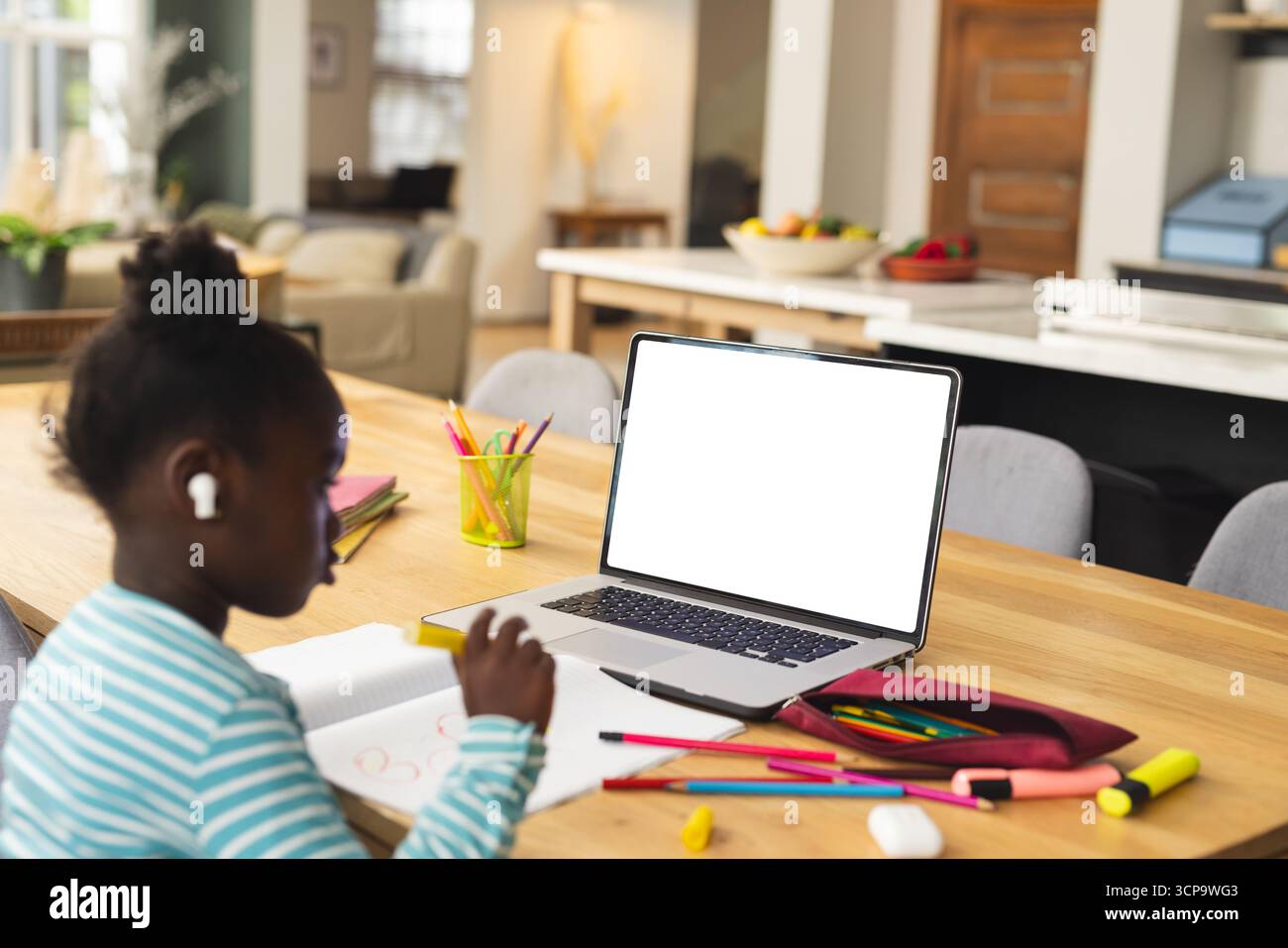Afroamerikanisches Kind, das zu Hause sitzt und sich mit Notizbuch, Bleistift und Laptop auf die Schularbeit konzentriert Stockfoto