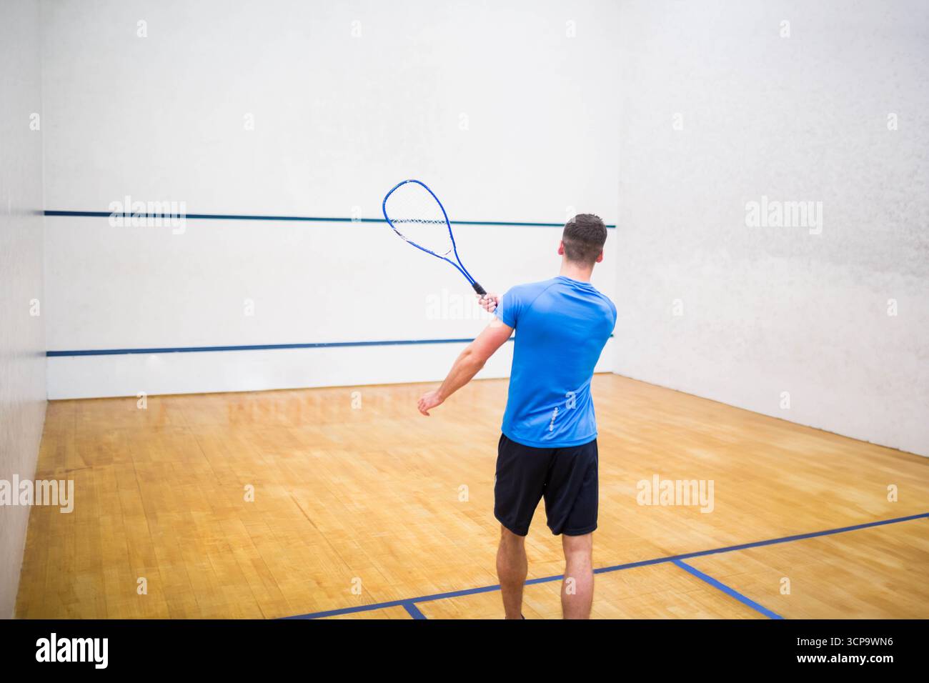 Squashspieler schwingen Schläger auf Holzboden und zielen gegen weiße Wand, die mit blauen Linien markiert ist Stockfoto