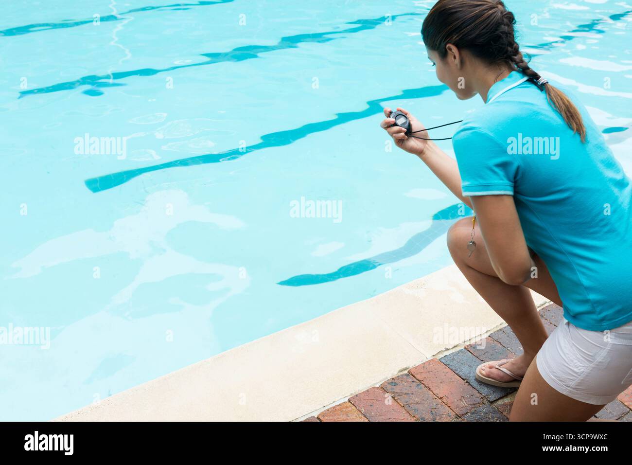 Weiblicher Badebus kniet auf der Poolterrasse im Freien und hält Stoppuhr an Fahrbahnmarkierungen, Kopierraum Stockfoto