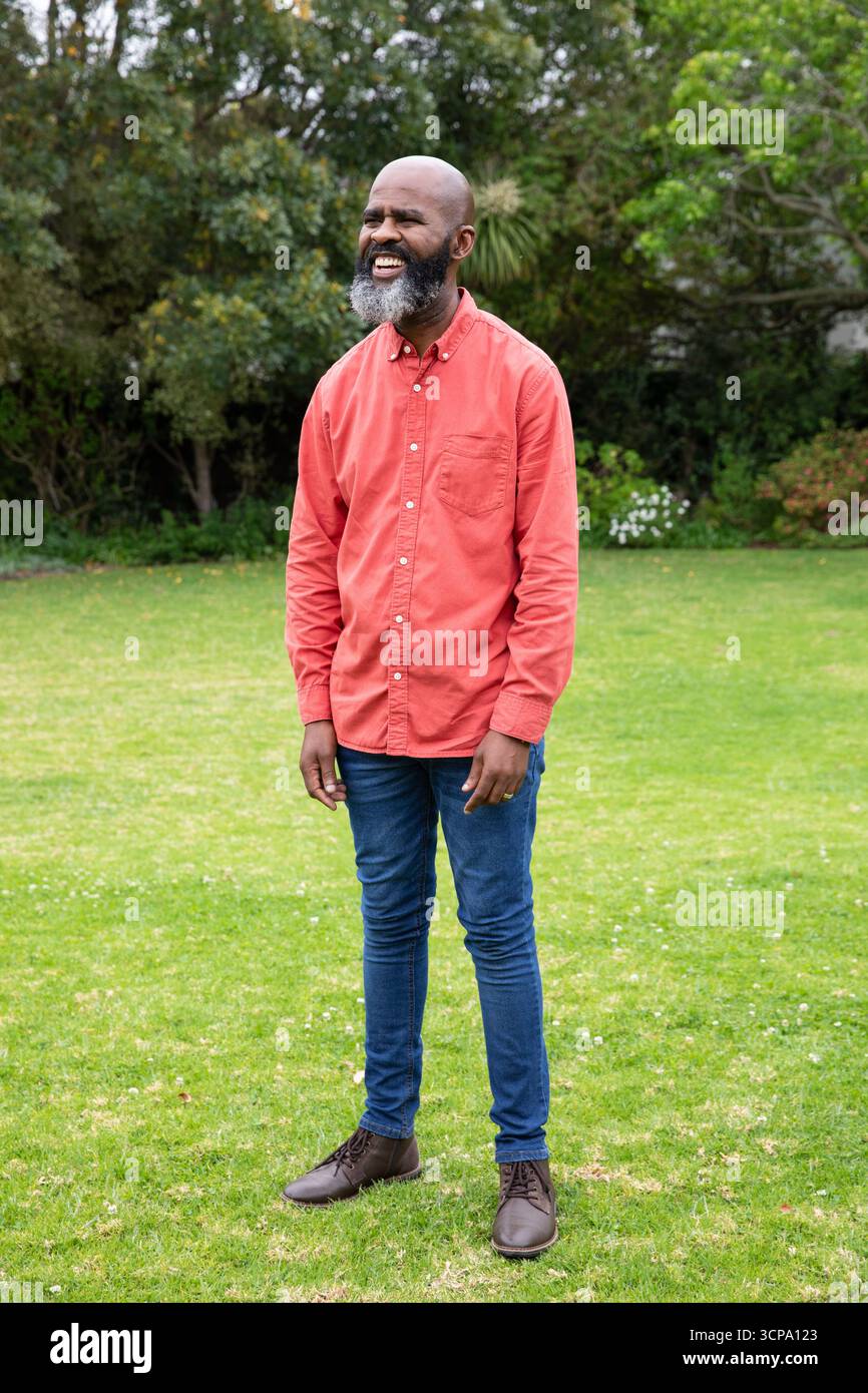 afroamerikaner, der im Garten steht, lächelt in rotem Hemd, blauer Jeans und Stiefeln Stockfoto
