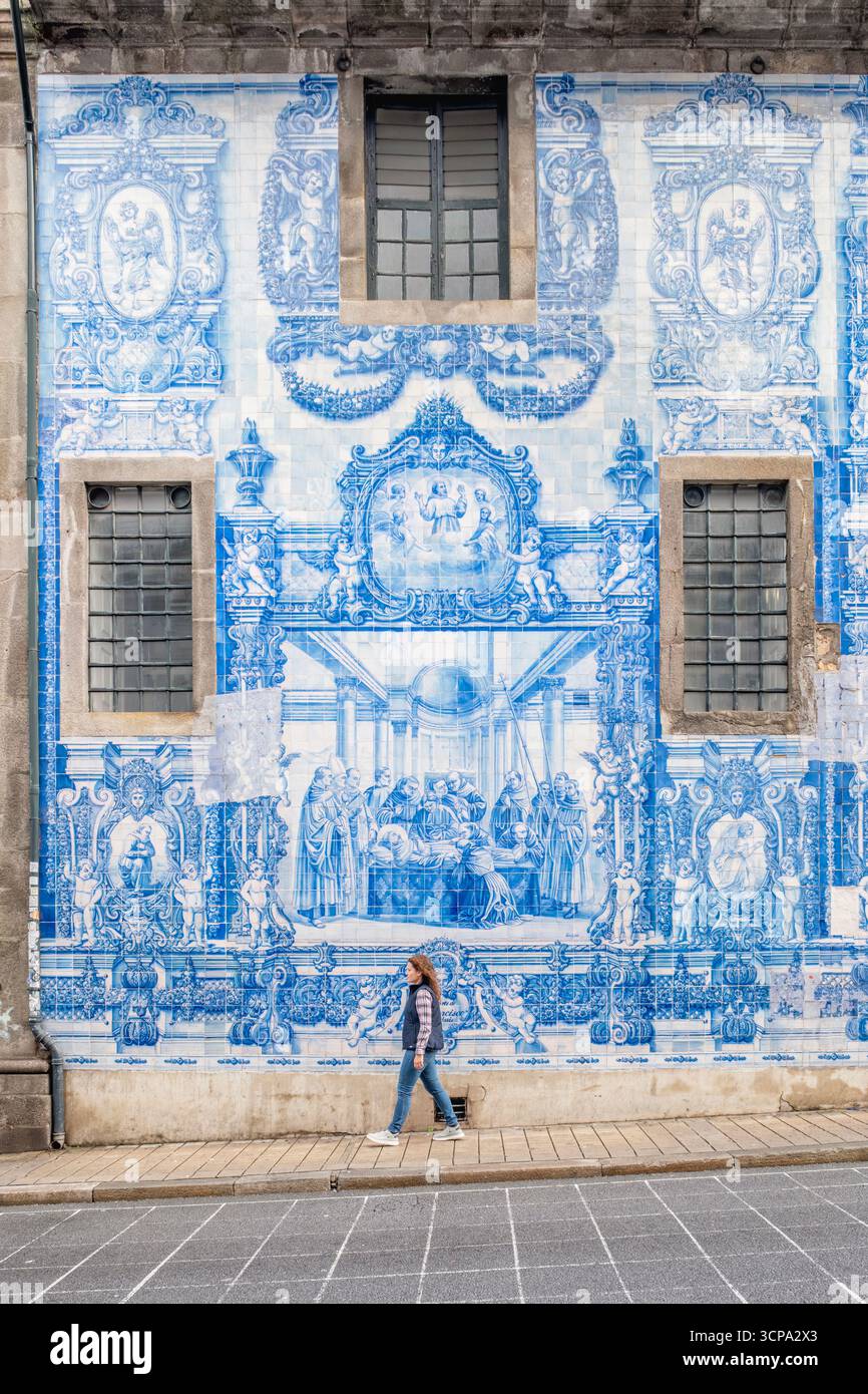 Junge Frau Schlendert Entlang Der Spektakulären Blauen Azulejo-Fassade Der Kirche Santo Ildefonso. Monumentale portugiesische Fliesenkunst, historische Architektur von Porto Stockfoto