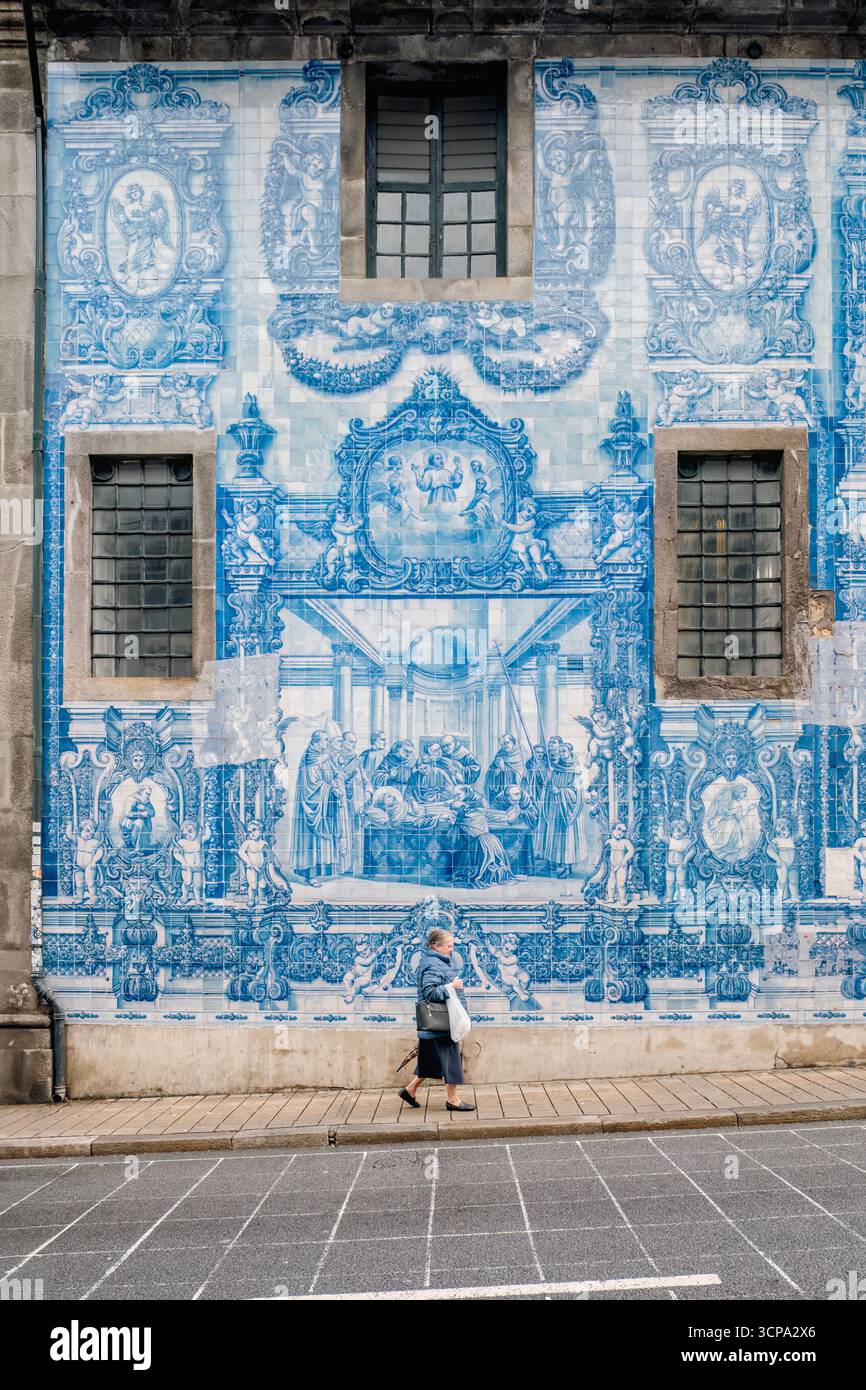 Ältere Frau, Die An Der Herrlichen Azulejo-Mauer Von Igreja Santo Ildefonso Vorbeiläuft. Traditionelle portugiesische Keramikkunst, Portos kulturelles Erbe auf der Straße Stockfoto