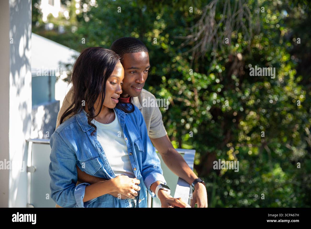 Afroamerikanisches Paar, das auf einem Metallgeländer am Balkon steht und Uhren trägt Stockfoto