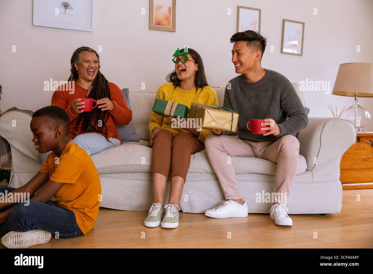 Verschiedene Familien tauschen Geschenke aus, während Kinder spielen und Erwachsene im Wohnzimmer aus Tassen schlürfen Stockfoto