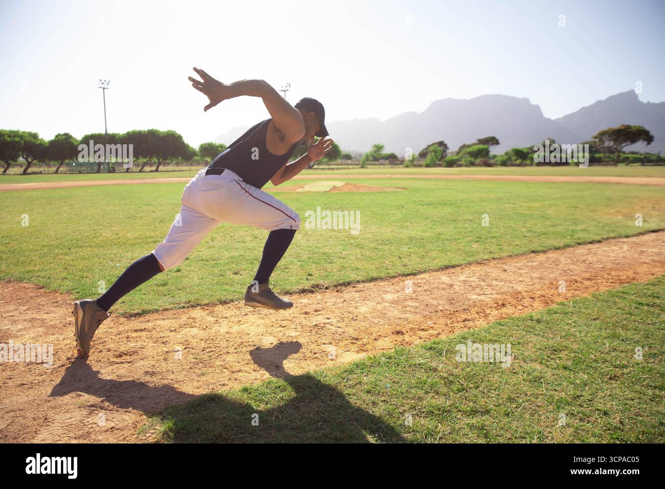 Männlicher Athlet sprintet auf Basepath auf Baseballdiamant vorbei an Gras und leichten Stangen, Kopierraum Stockfoto