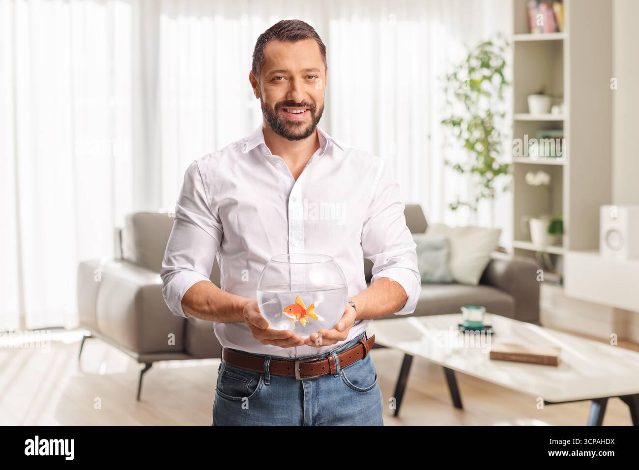 Ein Mann, der einen Goldfisch in einem Fischbecken hält, zu Hause in einem Wohnzimmer Stockfoto