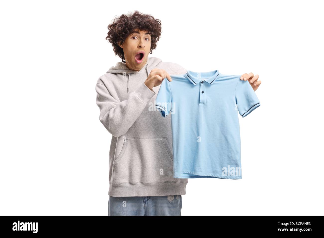 Schockierter Kerl, der ein kleines blaues T-Shirt auf weißem Rücken hält Stockfoto