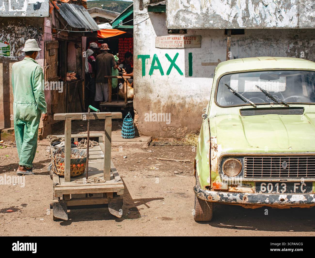 Ambositra, Madagaskar - 26. April 2019: Altes rostiges Auto parkt an einem sonnigen Tag neben der Hauptstraße, TEXTTAXI dahinter, Gruppe unbekannter Einheimischer im Hintergrund Stockfoto