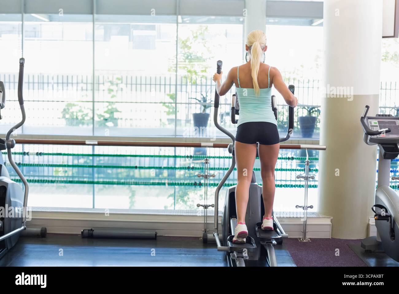 Weibliche Gymgoerin, die im Cardio-Bereich an den Fenstern mit Blick auf den Pool und die Pflanzen trainieren Stockfoto