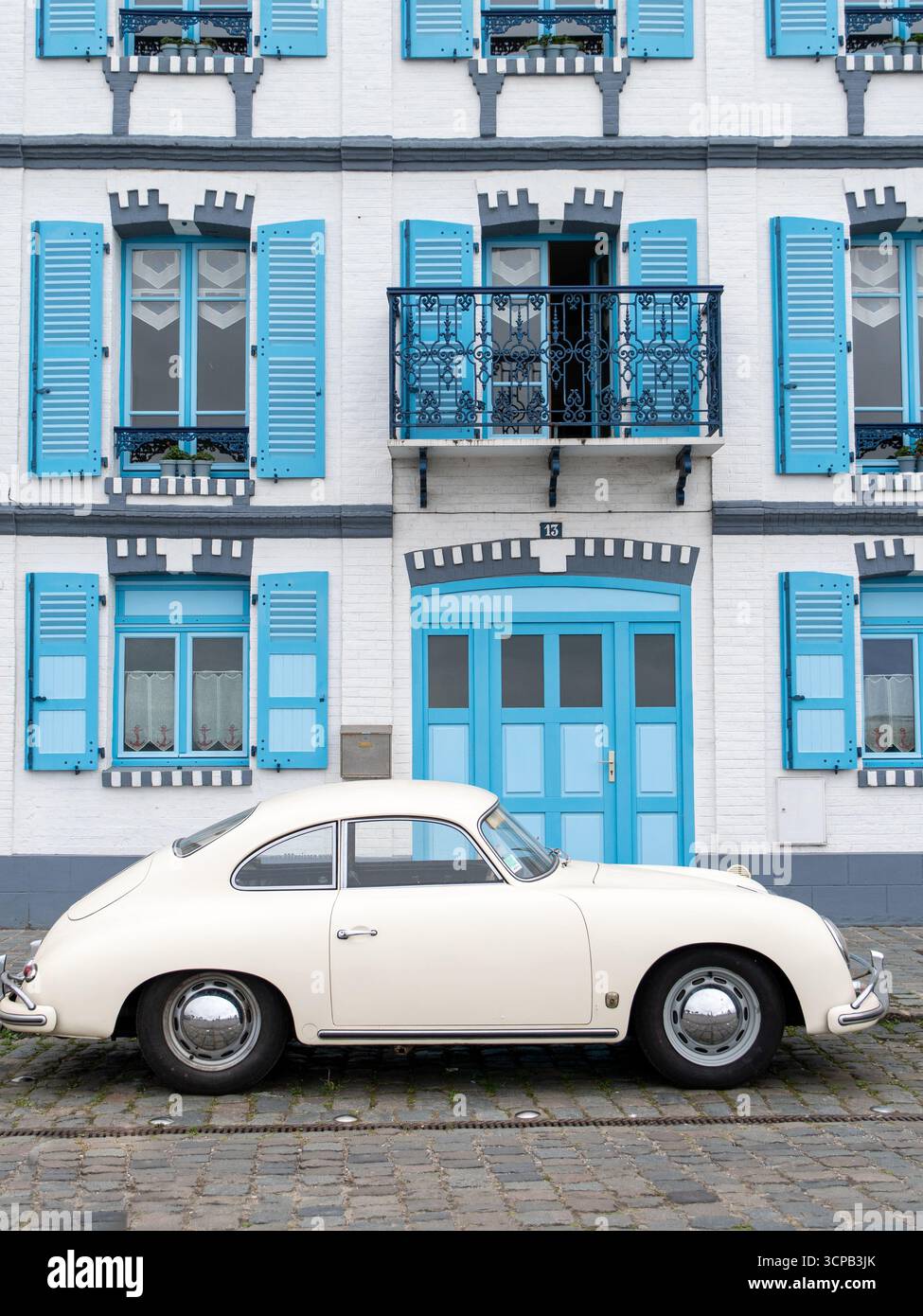 Ein makellos weißer Porsche 356 sitzt elegant vor einem bezaubernden Gebäude aus der französischen Kolonialzeit, das mit pulverblauen Fensterläden und kunstvoll verzierten Schmiedeeisen geschmückt ist Stockfoto