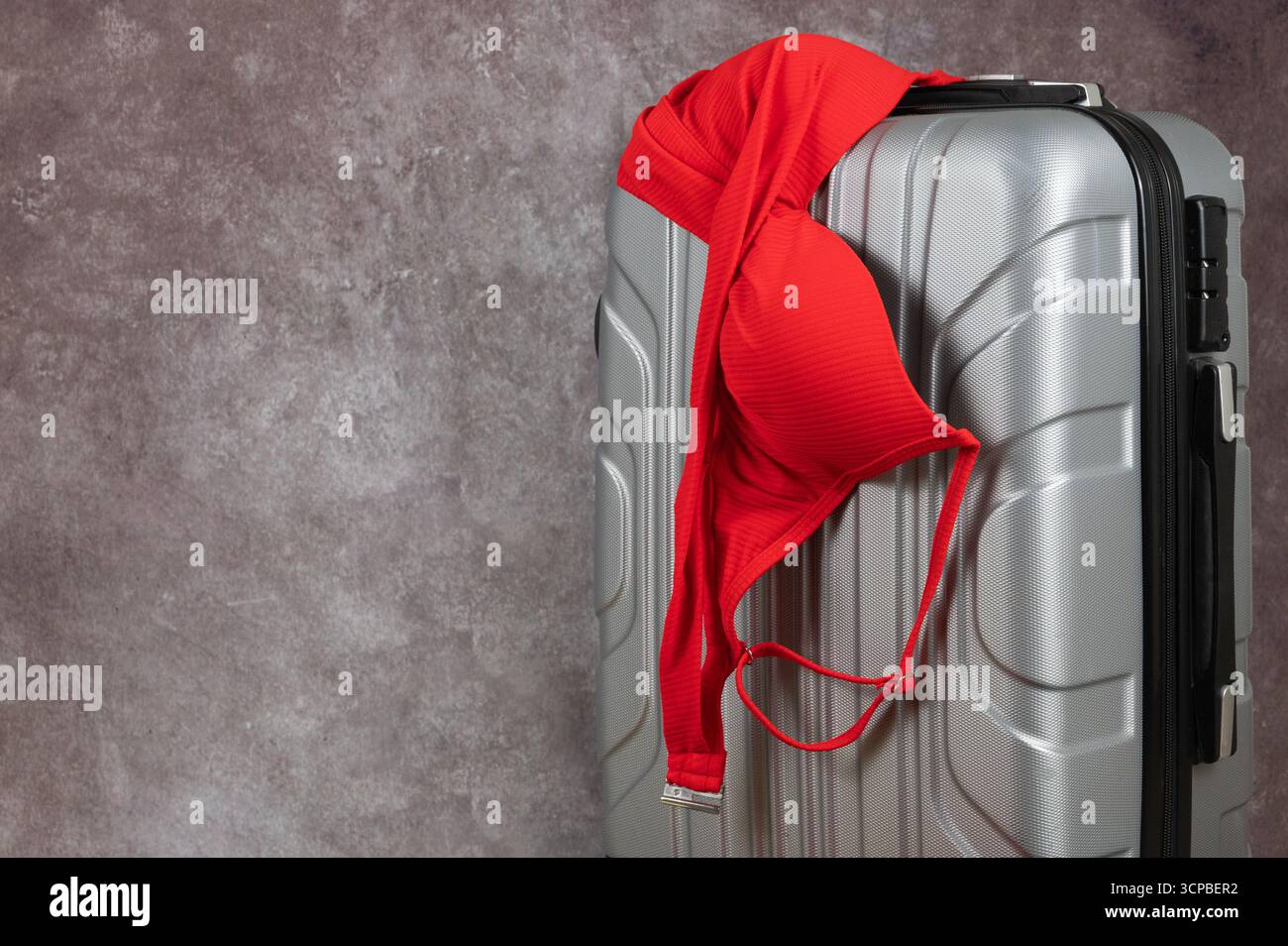 Ein leuchtend roter BH über einem glänzenden silbernen Koffer symbolisiert verspielte Reisen voller Freude und Abenteuer Stockfoto