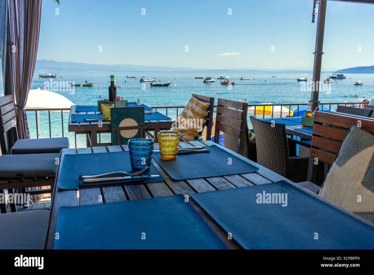 Seestrand-Café-Terrasse mit Tischen und Meerblick, Strandschirme und Boote in der Nähe Stockfoto